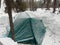 Green tent covered with snow in the forest in winter. Overnight in a tent in extreme conditions. Tourism for people of