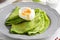 Green thin pancakes with spinach, poached egg, sour cream, lemon