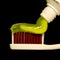 Green toothpaste on red toothbrush closeup