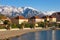 Green town at foot of snowy mountains. Montenegro, view of embankment of Tivat city and Lovcen mountain on sunny winter day