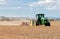 A green tractor in a farm field plowing the ground for planting.