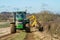 Green tractor hedge cutting and digger clearing a ditch