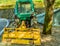 Green tractor parked under a large shade tree