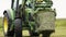 Green tractor picks up stack of grass with metal arms at farm field