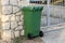 Green trash can by the gates of the house