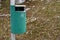 Green trash can on metallic pole with grass and snow background