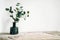 Green tree Branch putted into black glass vase on the natural stone mantel shelf on the white color wall background lit with side