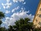 A green tree and a vintage brick multi-apartment five-story house in the sun against a blue sky with white clouds. Photo