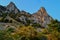 Green trees and bushes grow on steep side of mountain with sharp rocks, peaks in warm orange sunset light. Simeiz