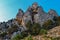 Green trees and bushes grow on steep side of mountains with sharp rocks, peaks in warm orange sunset light. Crimea