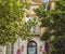 Green trees cover vintage home facade with stone flower vases and hanging lights