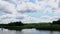 Green trees by the lake on a sunny day, with clouds on the sky