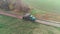 A green truck is dumping gravel on the countryside road, aerial shot