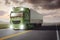 Green truck with a trailer driving on a remote highway through a landscape at dusk