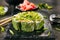 Green uramaki sushi roll with rice, cream cheese, fried salmon, tomatoes, beijing cabbage, green onion, dill and spicy sauce close