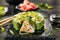 Green uramaki sushi roll with rice, cream cheese, fried salmon, tomatoes, beijing cabbage, green onion, dill and spicy sauce close