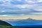 Green valley covered with clouds with smoking volcanoes in background