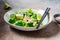 Green vegan salad with broccoli, smoked tofu and tahini dressing in white bowl, dark background