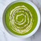 Green vegetable cream soup in a white bowl on a gray concrete background top view.