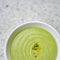 Green vegetable cream soup in a white bowl on a gray concrete background top view.