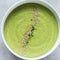 Green vegetable cream soup in a white bowl on a gray concrete background top view.