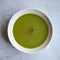 Green vegetable cream soup in a white bowl on a gray concrete background top view.