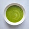 Green vegetable cream soup in a white bowl on a gray concrete background top view.