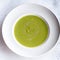 Green vegetable cream soup in a white bowl on a gray concrete background top view.