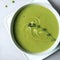 Green vegetable cream soup in a white bowl on a gray concrete background top view.