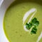 Green vegetable cream soup in a white bowl on a gray concrete background top view.