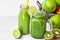 Green vegetable smoothie in glass mug and fruit juice in bottle with straw, basket with apples, lime, kiwi