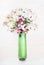 Green Vial with organic botanical cosmetic product and flowers and herbs bunch on white wooden background, top view.