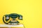 Green vintage corded phone on table against yellow background. Space for text