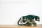 Green vintage corded phone on wooden shelf near wall. Space for text