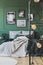 Green wall with gallery of poster in trendy bedroom interior with double bed