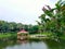 Green water of the pond with the little hut/ tukul in the middle surrounded by trees and bushes in beautiful bangladeshi park in