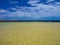 Green water in a quiet bay near the ocean. Coast of black volcanic rock. Glare on the water. Waves from the breeze. Light wind