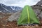 Green waterproof and windproof tent for hiking is in mountains at windy weather, standing behind big stone for protection from the