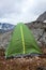 Green waterproof and windproof tent for hiking is in mountains at windy weather, standing behind big stone for protection from the