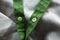 green webbing braid with button clasp on a background of light gray fabric