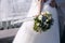 Green and white wedding bouquet in hands of the bride with a fluttering in the wind blue lace ribbon