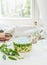 Green wild garlic soup in glass cooking pot stay on light table with ingredients at window background. Seasonal home cuisine.