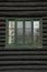 Green window and rough black painted logs on an old log cabin bu