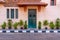 Green wooden door with red tile canopy above and green window shutters on stone bricks wall