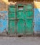 Green wooden grunge weathered abandoned door on dirty wall painted in yellow and blue