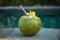 Green young coconut close up with bamboo straw and tropical flower frangipani on the edge of swimming pool