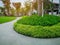 Greenery bush and trees in garden with gray curve pattern walkway, sand washed finishing on concrete paving and brown gravel