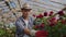 Greenhouse with growing roses inside which A male gardener in a hat inspects flower buds and petals. A small flower