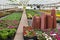 A greenhouse with many flowers in boxes and flowerpots, in the foreground a bunch of brown flowerpots standing in stacks