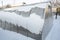 Greenhouses under the snow. Snow on the roof of the greenhouse. A polycarbonate greenhouse for planting vegetables stands during